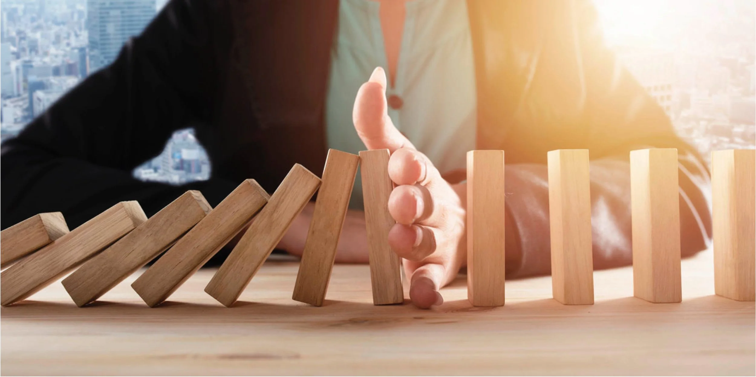 A person failing to stop wooden blocks from toppling over, illustrating a domino effect.