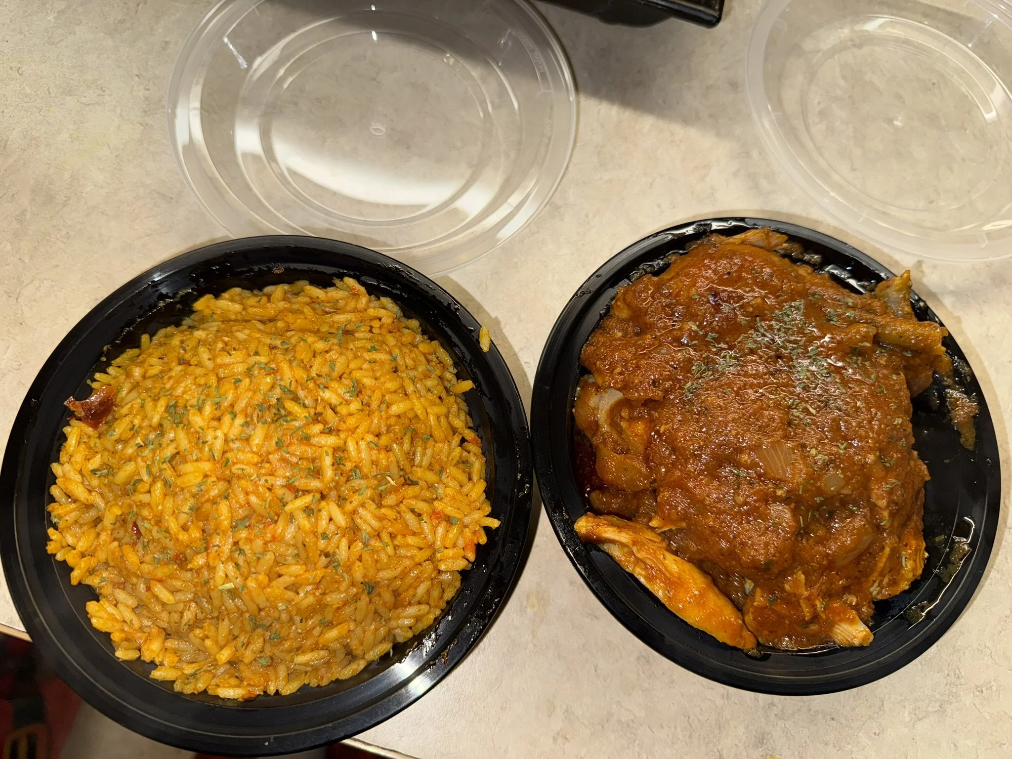 Two black plastic containers with clear plastic lids containing Mexican food. The left container has yellow rice with cilantro, and the right container has beef or chicken topped with red enchilada sauce with onions and possibly chicken or beef under