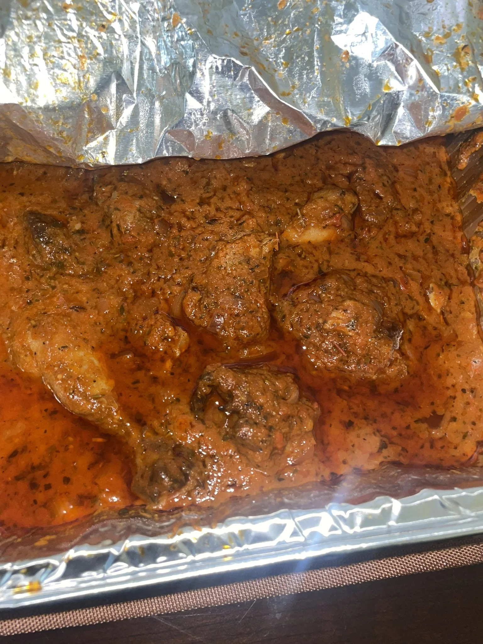 Raw chicken coated in spicy red sauce inside a foil-lined baking dish.