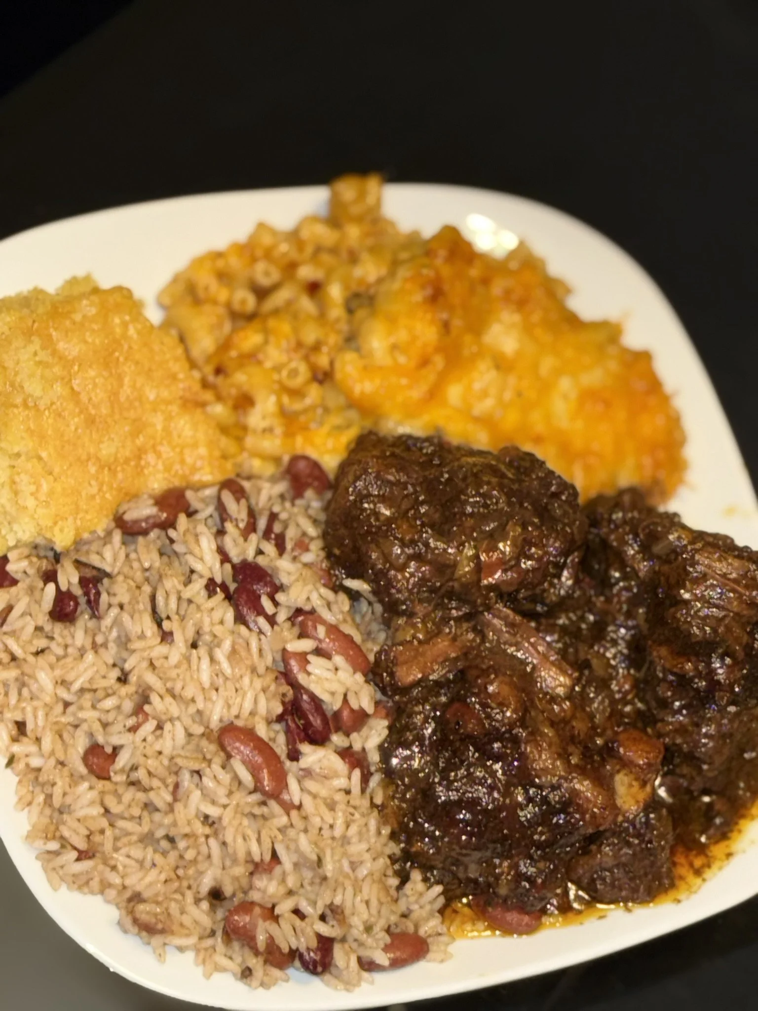 Plate of cooked rice with beans, fried chicken pieces, macaroni and cheese, and barbecue ribs.