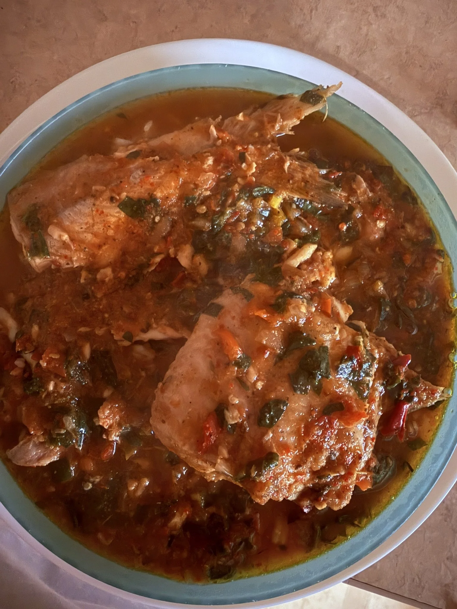 Two cooked fish in a spicy tomato-based sauce with herbs and vegetables in a bowl.