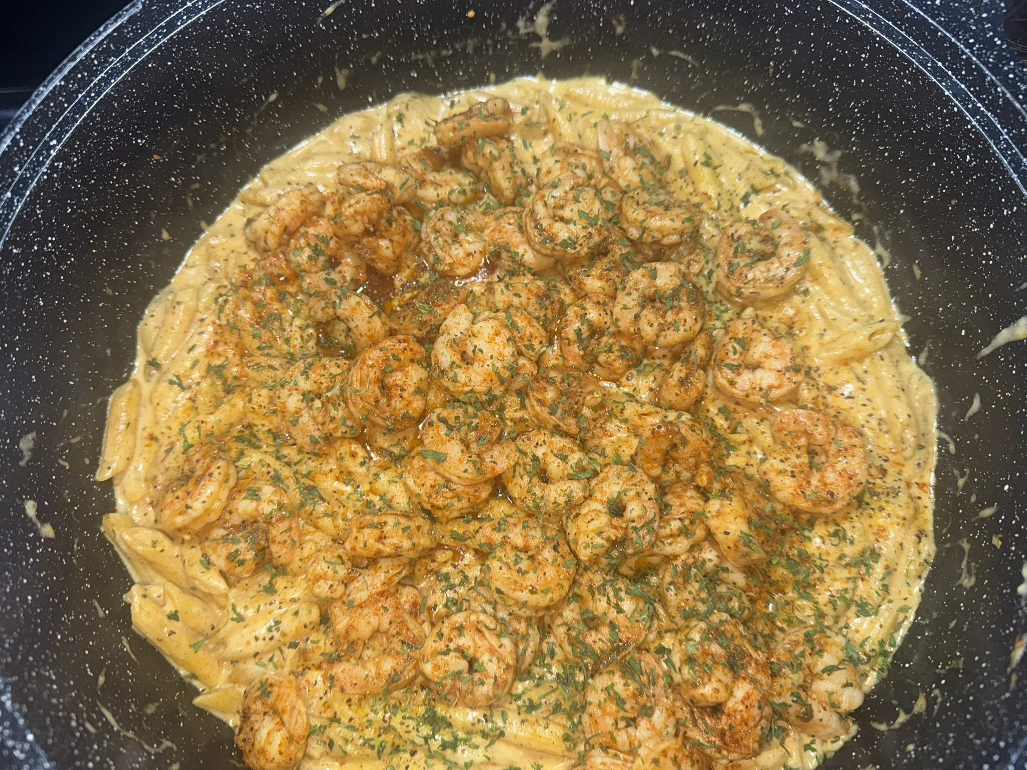 Shrimp and pasta in a creamy sauce with herbs in a black pan.