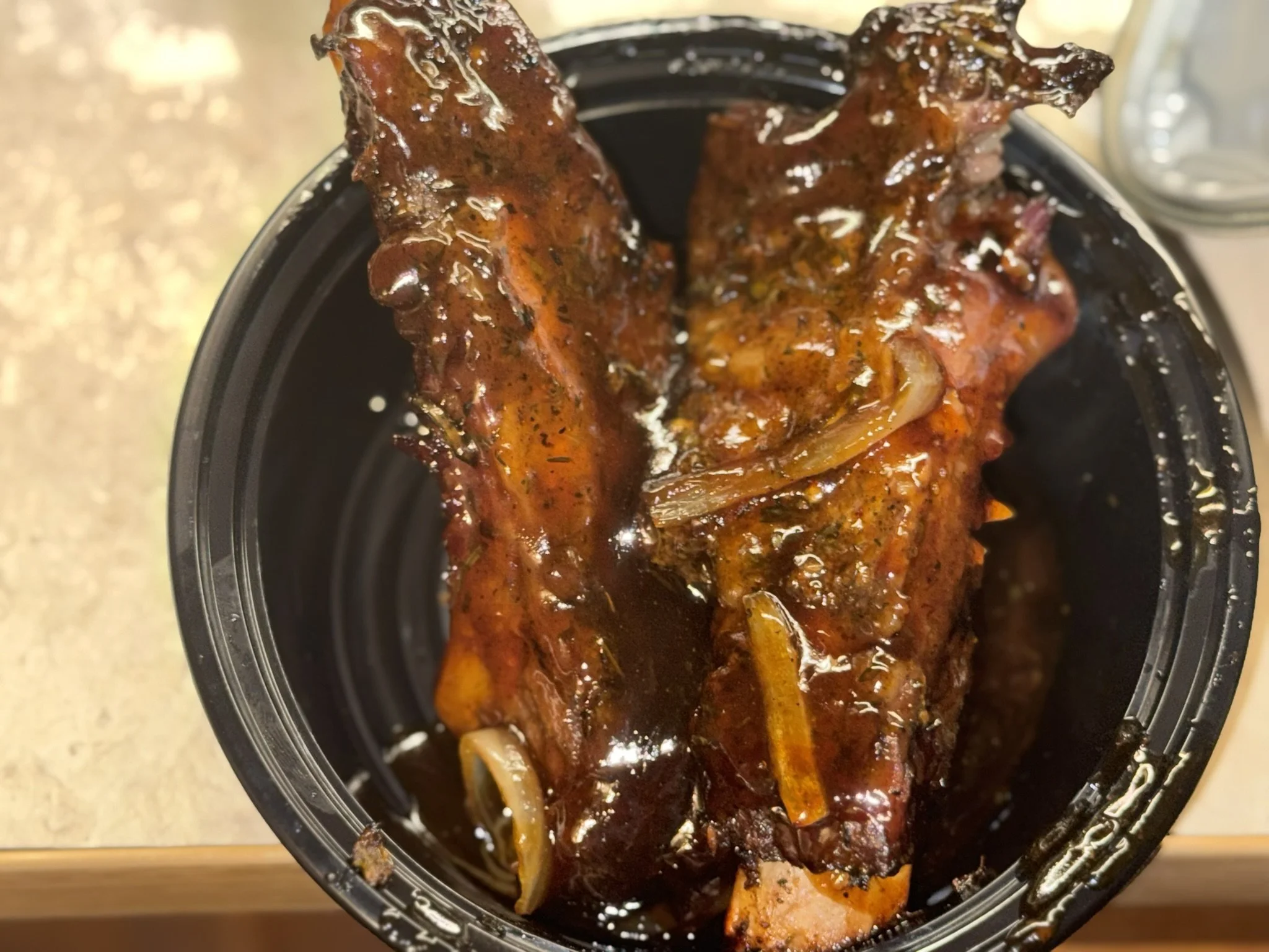 Barbecue pork rib with sauce inside a black plastic container.