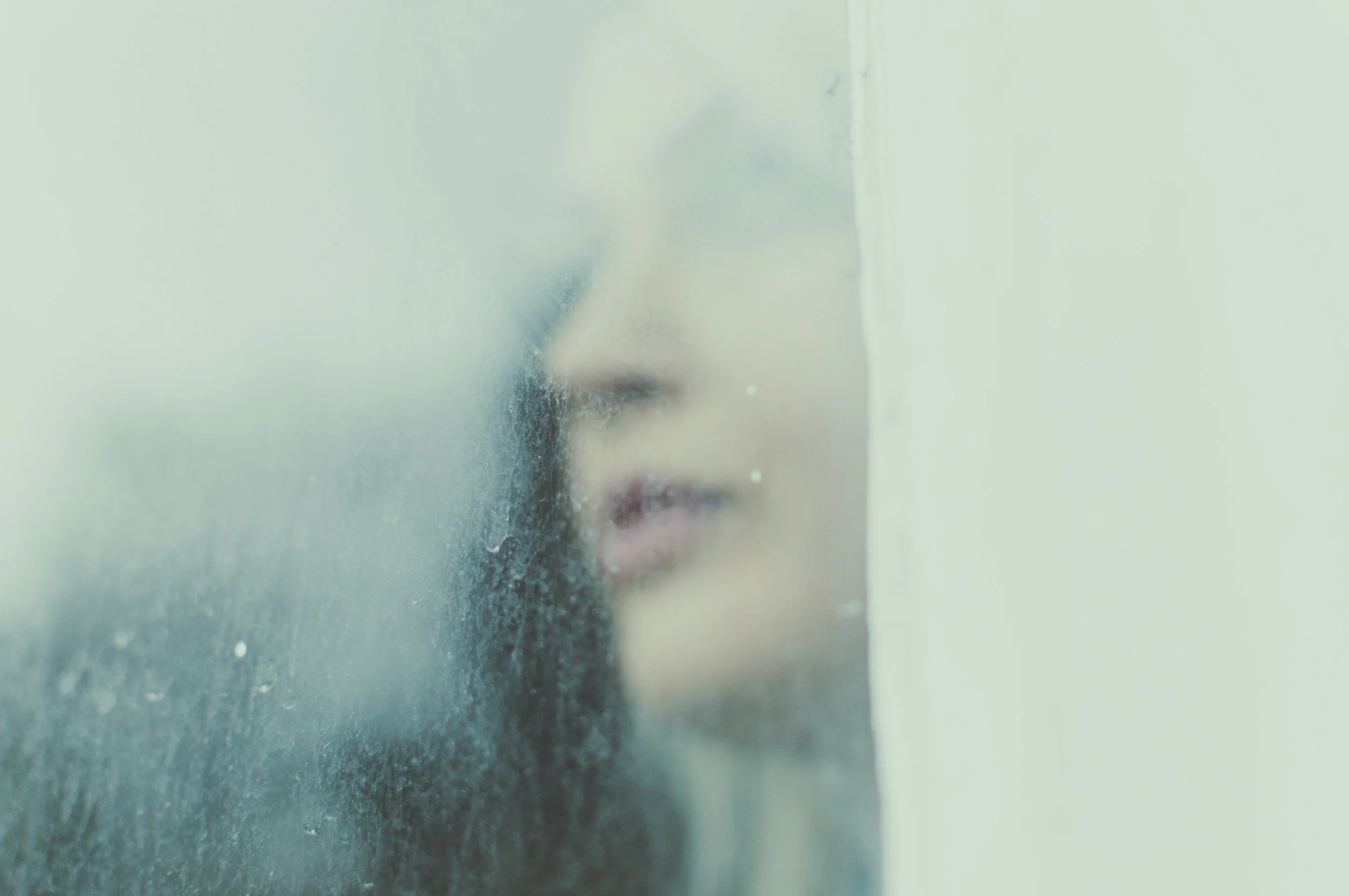 A person's face seen through a foggy or dirty glass surface, with their nose and lips partially visible.