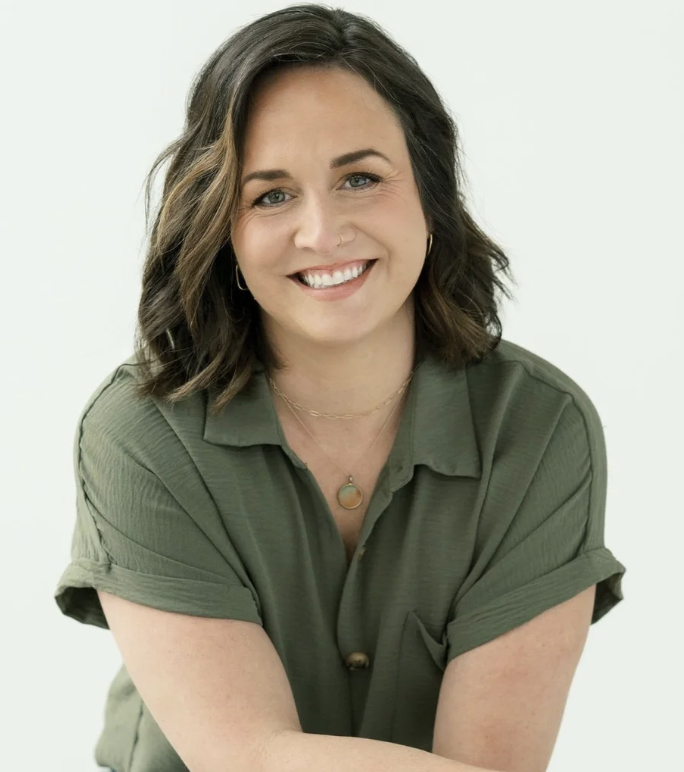 A woman with shoulder-length brunette hair, smiling and wearing a white top, set against a pink circular background.