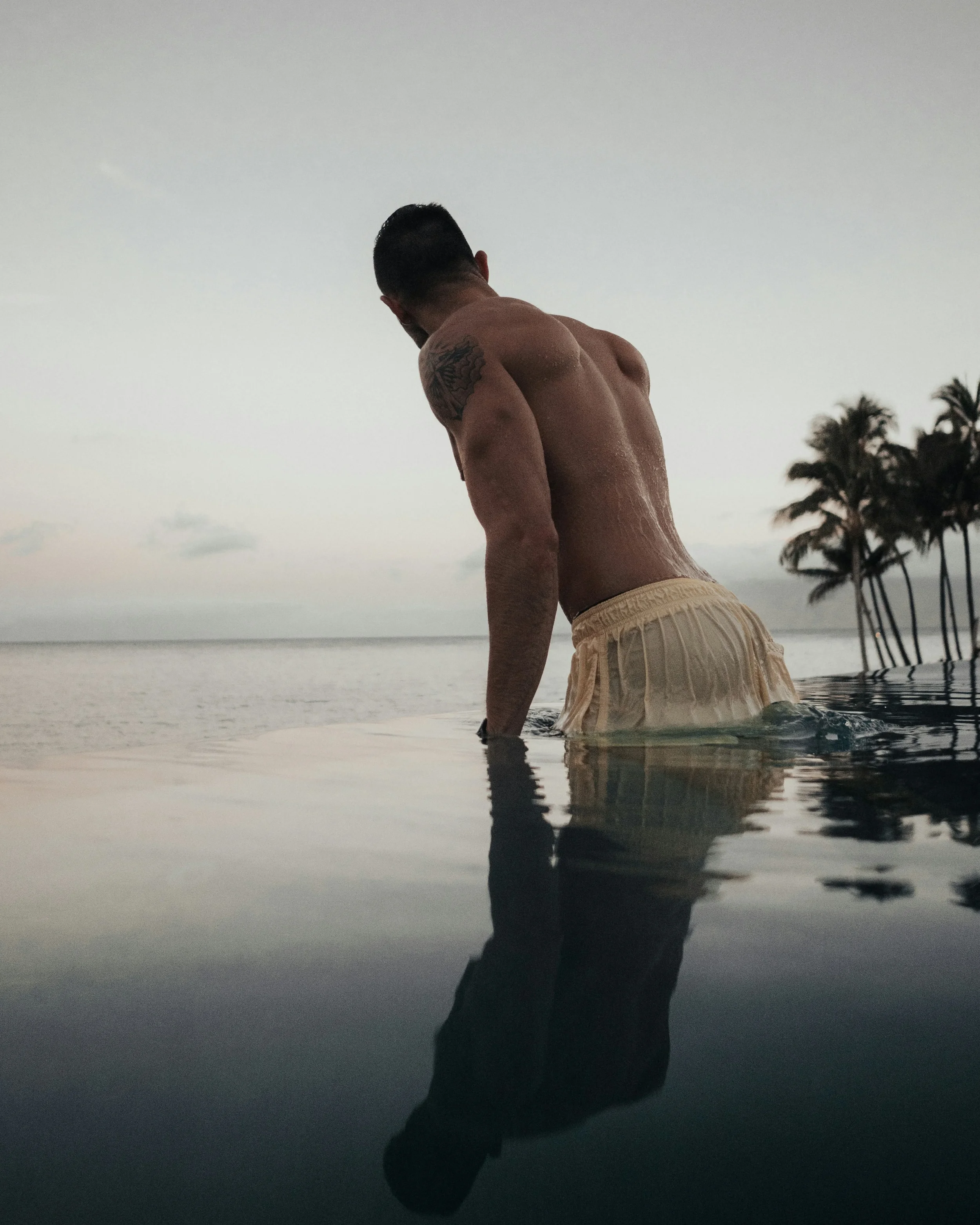 photo-of-a-shirtless-man-in-a-bathing-suit-lifting-himself-out-of-an-infinity-pool-at-sunset.