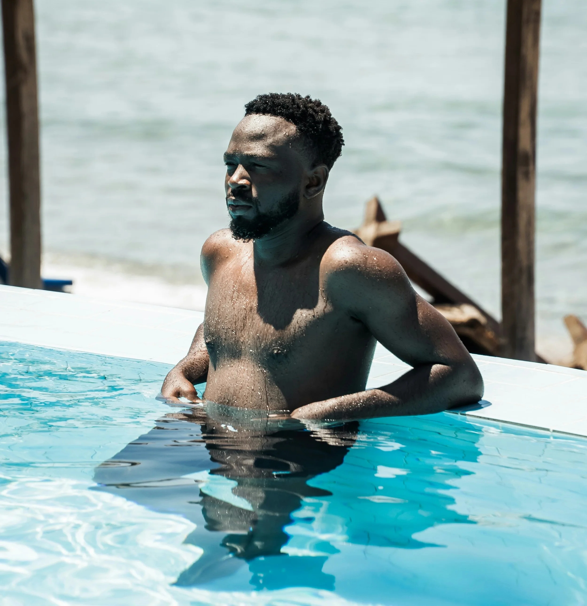 photo of a shirtless man sitting half submerged in an outdoor pool
