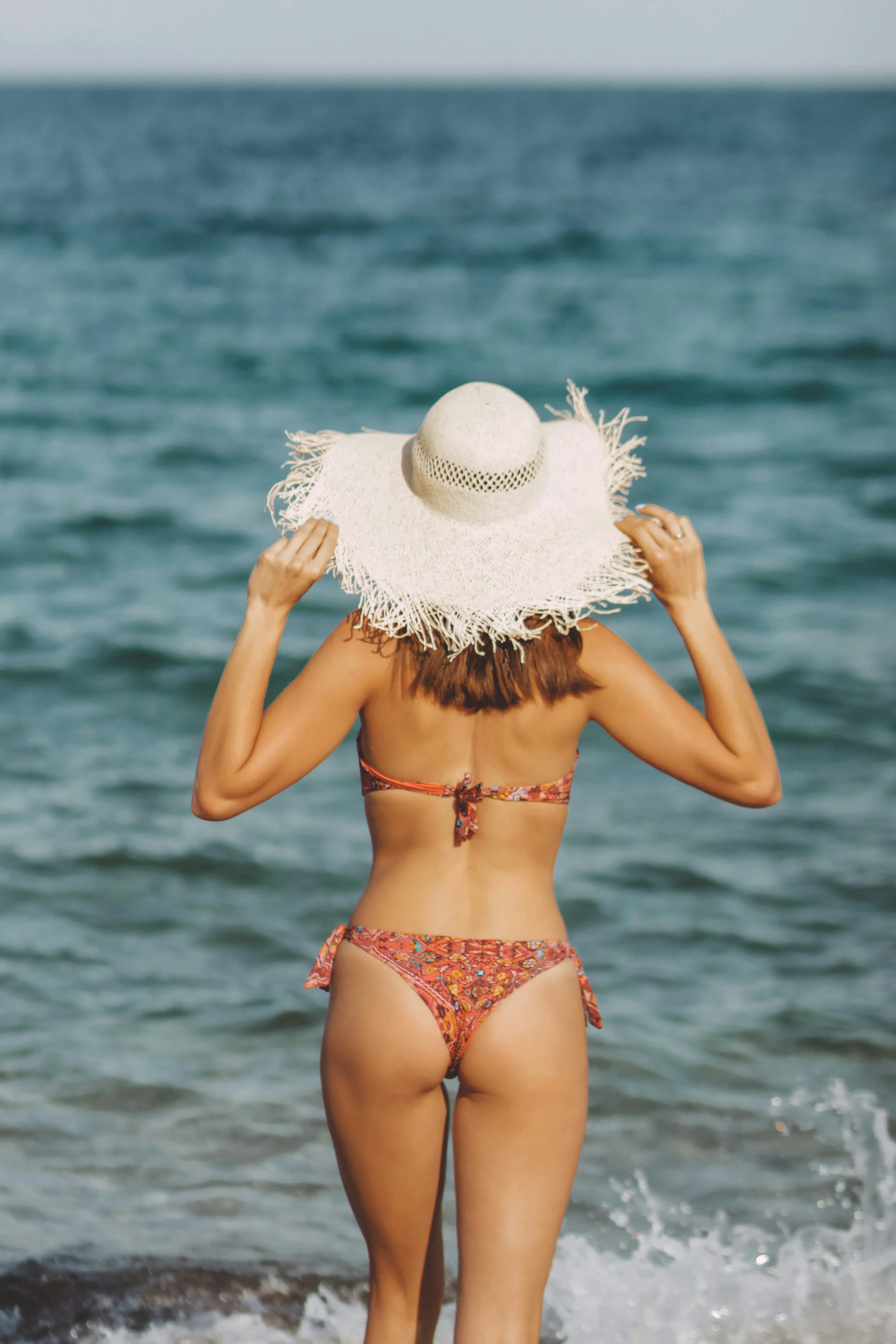 photo-of-a-person-wearing-a-bikin-and-sunhat-wading-into-the-ocean