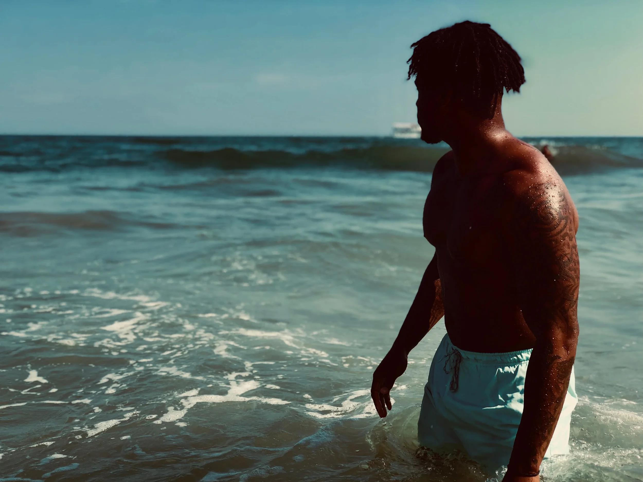 photo-of-a-shirtless-man-looking-at-the-ocean-while-strolling-along-a-beach