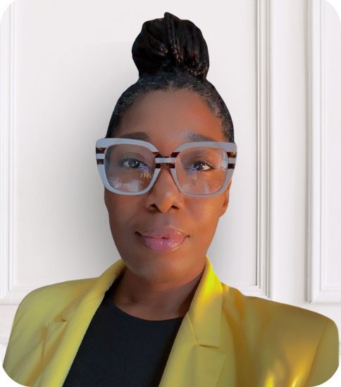 A woman with her hair styled in a high bun, wearing large glasses, a yellow blazer, and a black top, standing in front of a white door.