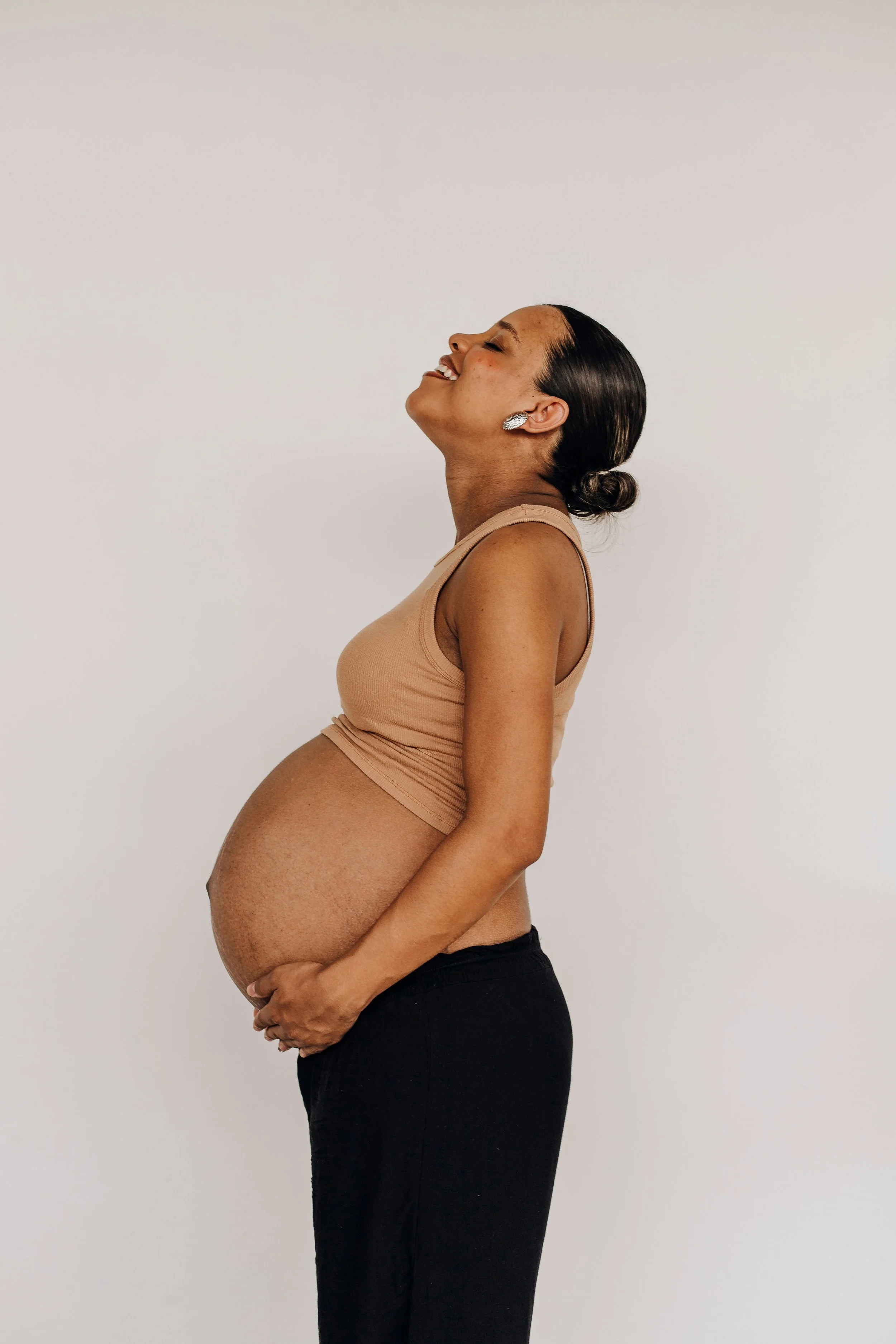Close-up of a pregnant woman's belly with her hands gently holding it, wearing a black top and black pants.
