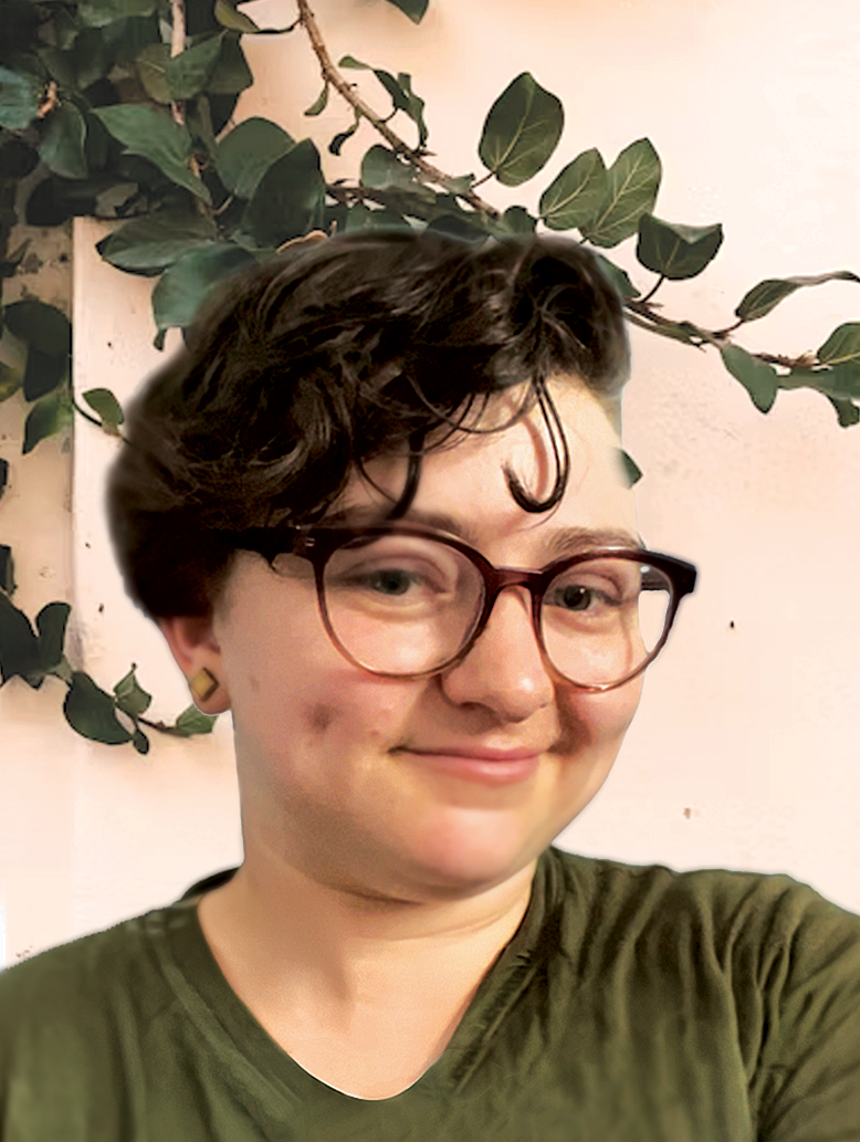 A person with short dark wavy hair and glasses smiling, standing in front of a leafy vine plant on a white wall.