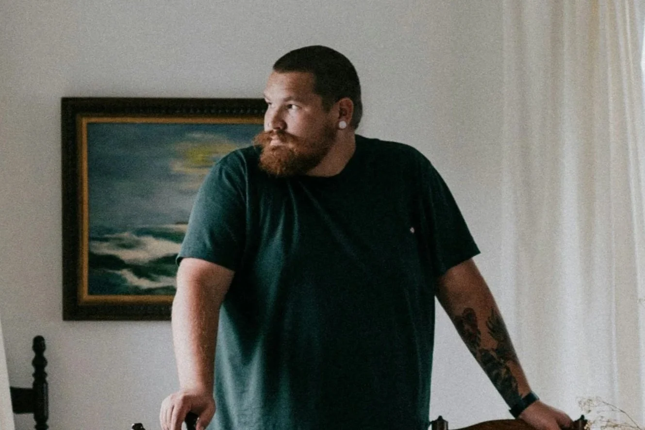 Silhouette of a shirtless person with short hair and a necklace, facing to the left, with shadows cast on a wall behind him.