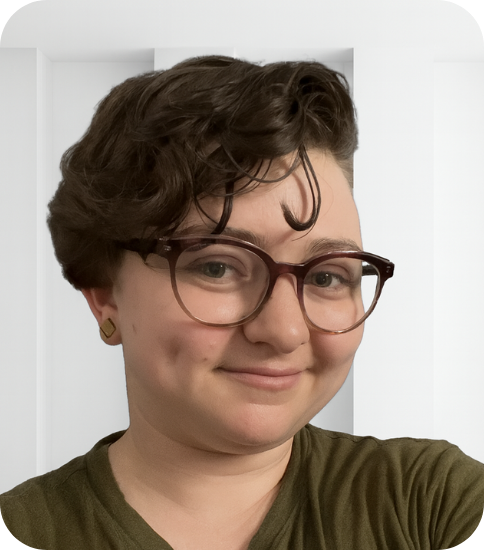 A person smiling with short curly hair, wearing glasses and a green shirt.