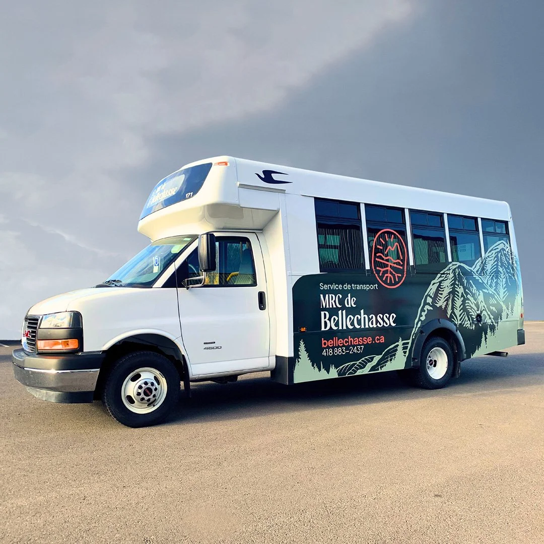 Minibus blanc avec décor montagne et forêt, logo et texte pour le service de transport MRC de Bellechasse, site internet bellechasse.ca, numéro de téléphone 418 883-2437.