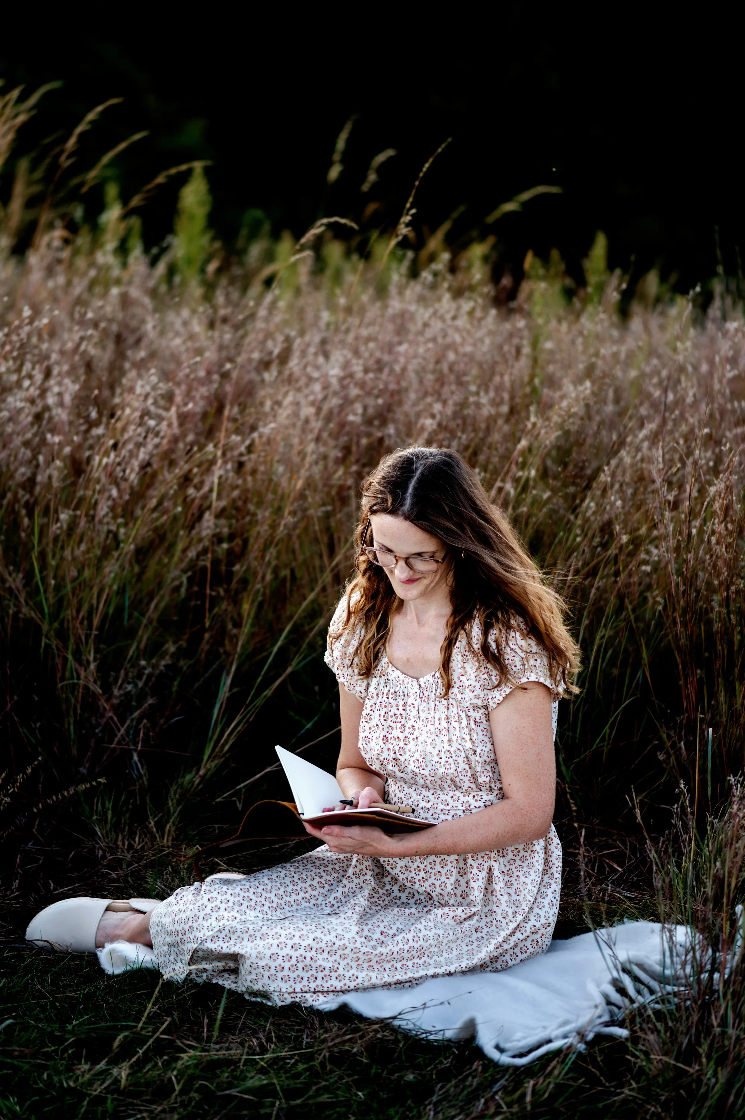 Woman sitting on a blanket in a field writing in a journal