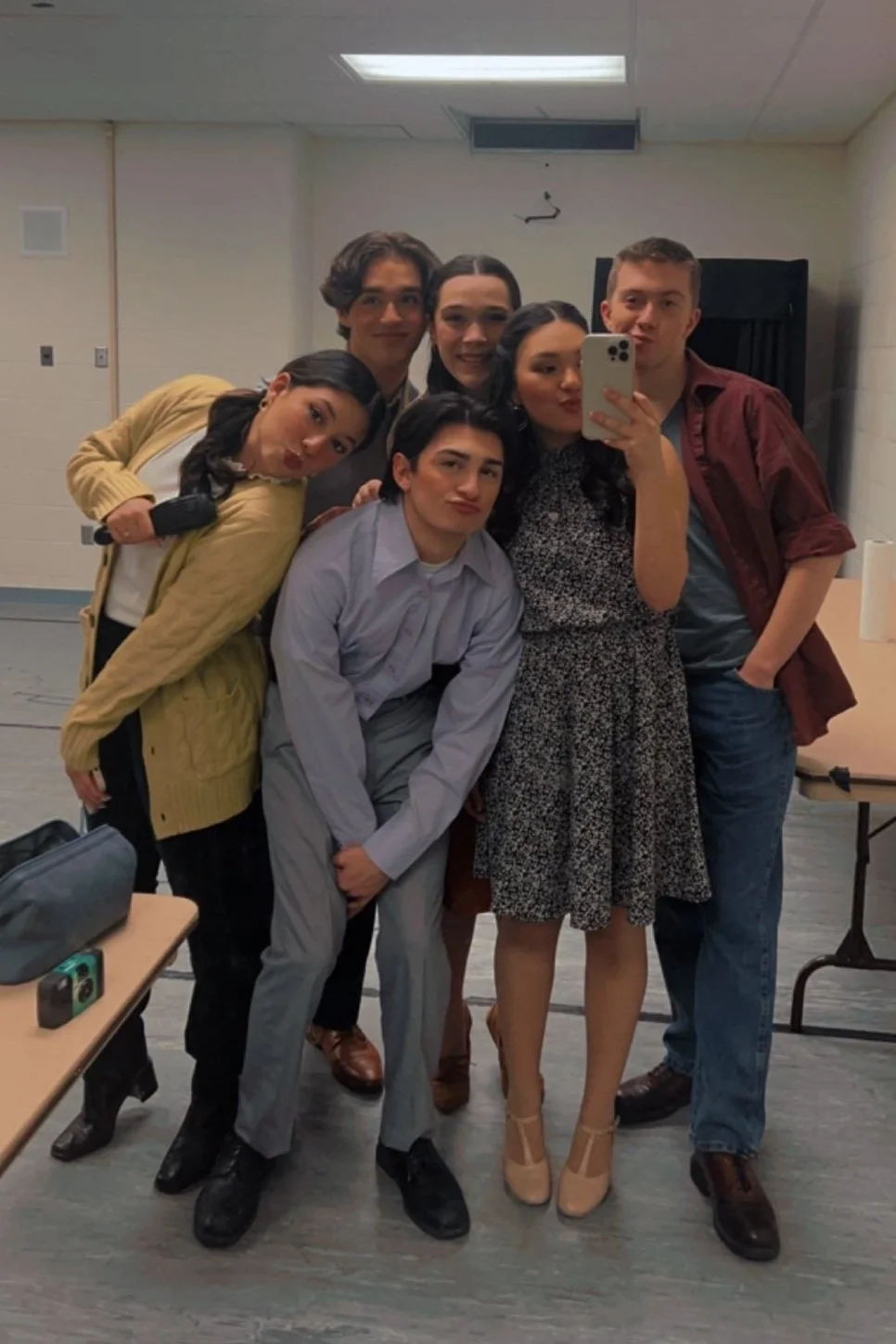 Group of six young people taking a mirror selfie in a room, posing closely together and making playful facial expressions.