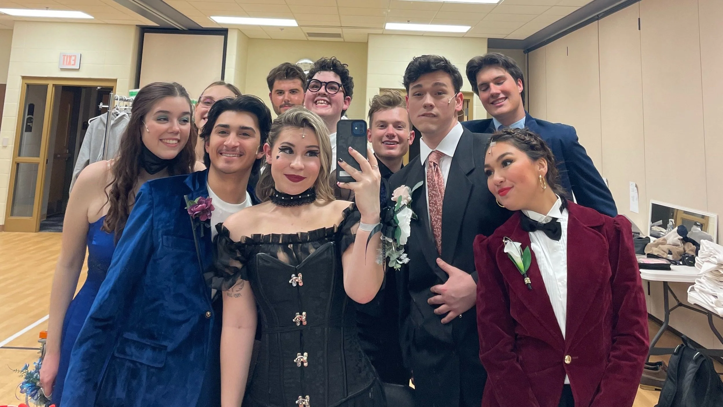 Group of teenagers dressed in formal attire taking a selfie in a dressing room.