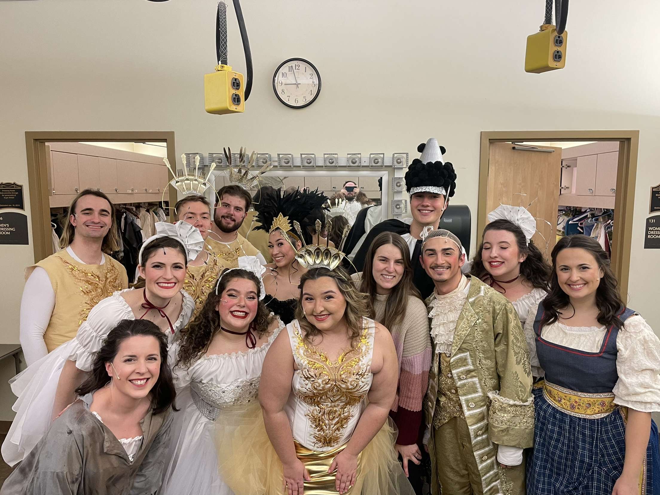 Group of young performers dressed in theatrical costumes poses backstage, smiling