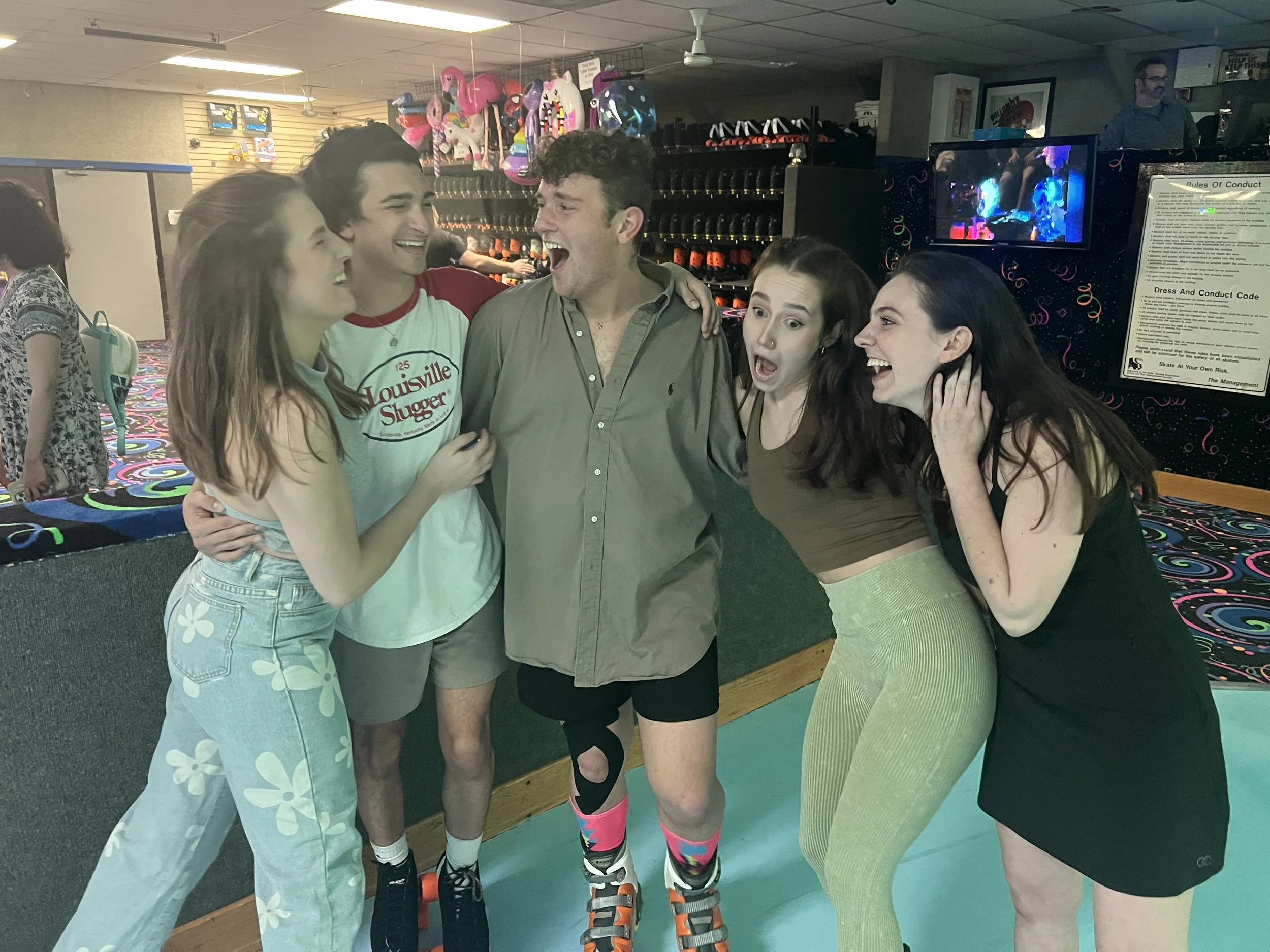 Group of five young adults laughing and enjoying themselves at a roller skating rink, with colorful shoes and casual attire.