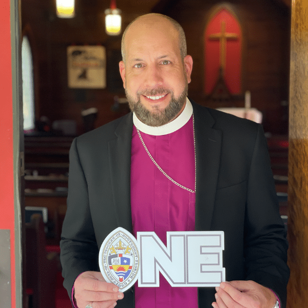 A man dressed as a bishop in a church holding a sign that says 'ONE' with a religious emblem.