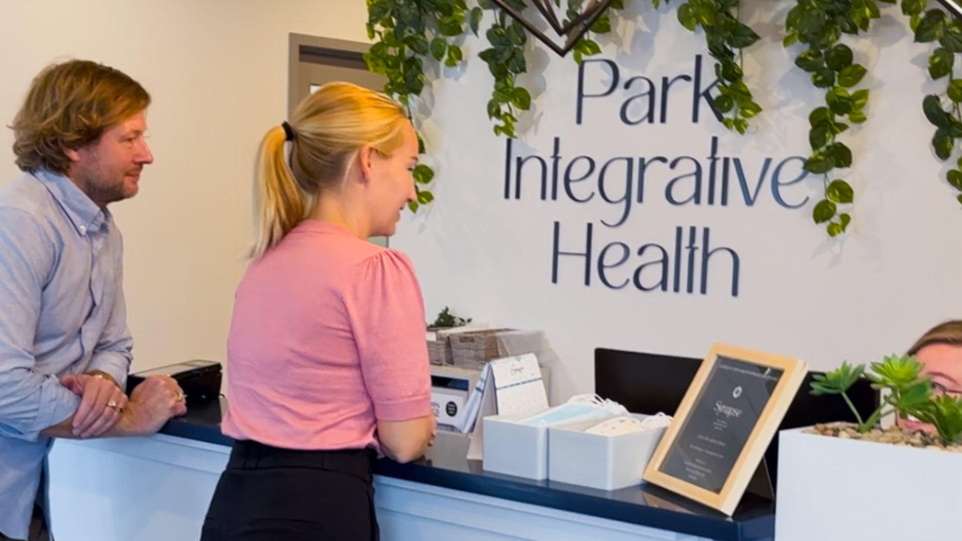 Co-founders of Park Integrative Health, Brandon Jacobs and Heather Gazley talk to their team member in front of the Park Integrative Health logo sign.
