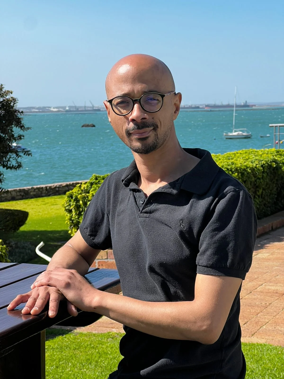 Person with short dark hair, wearing a sports jersey with a pattern of gender symbols, standing with arms crossed against a gray background.