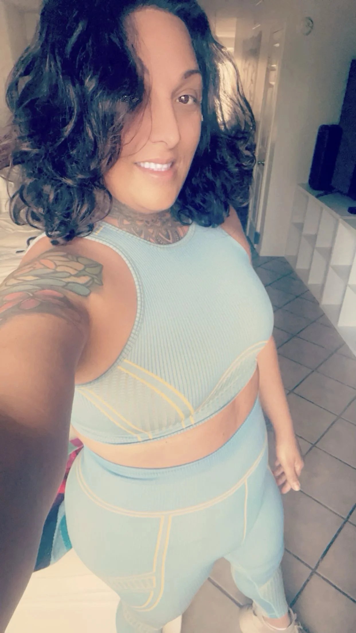 Young person with long curly blonde hair wearing a red cap with white patterns and a yellow shirt outdoors on a sunny day.