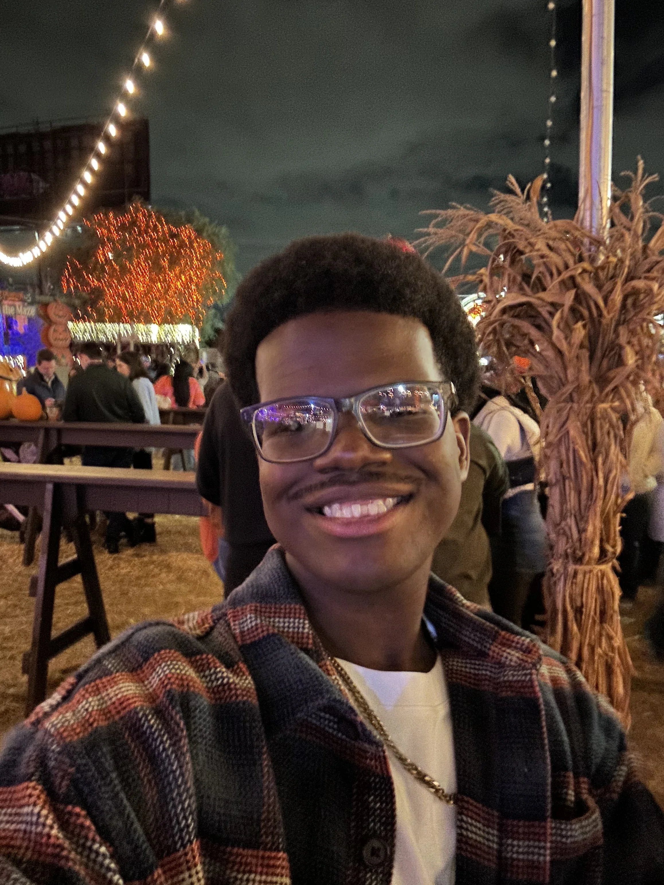 Young man in formal suit and striped tie smiling, with a blurred person in the background.