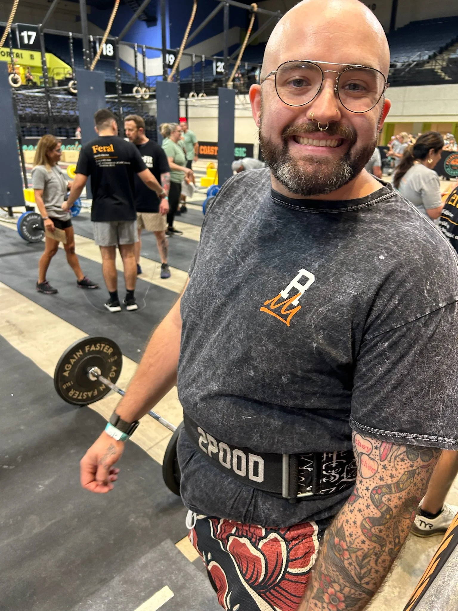 A young man with curly hair and glasses smiling outdoors during sunset, with mountains and trees in the background.