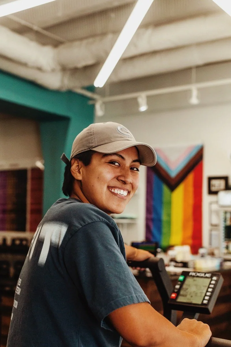 Smiling young man with glasses and black cap in lush green tropical foliage.