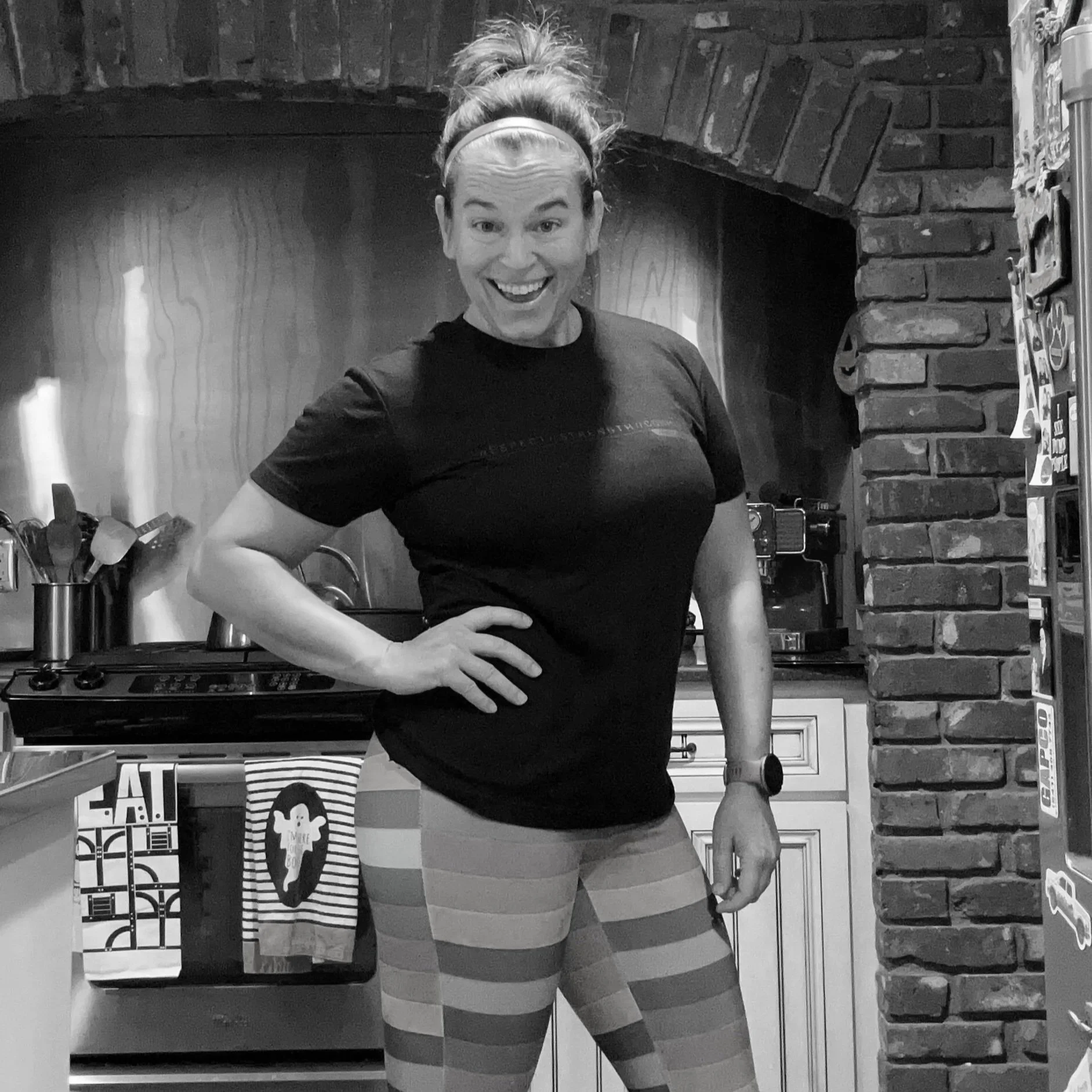 A black and white photo of a woman with shoulder-length hair, smiling, wearing earrings and a patterned blouse, sitting in a car.