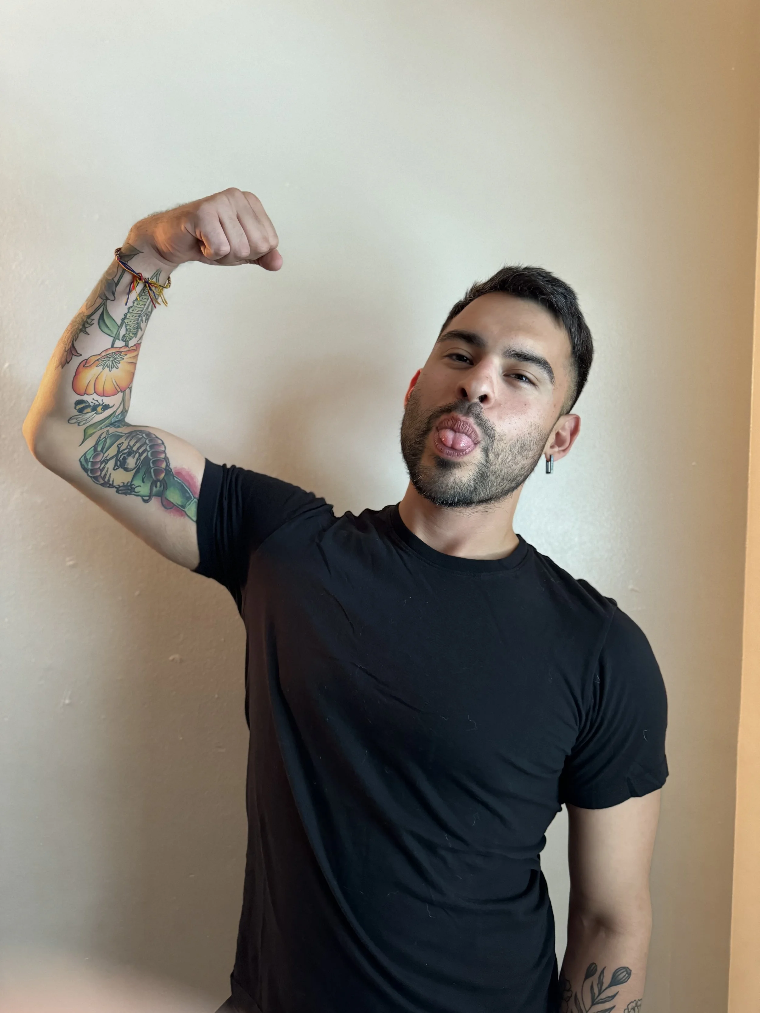 A shirtless person with tattoos standing in front of a dark background, with a neon sign that reads 'Bathroom' visible to the left.