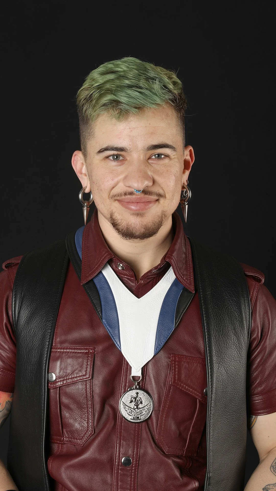 A person squatting by a river with mountains and trees in the background, smiling at the camera.