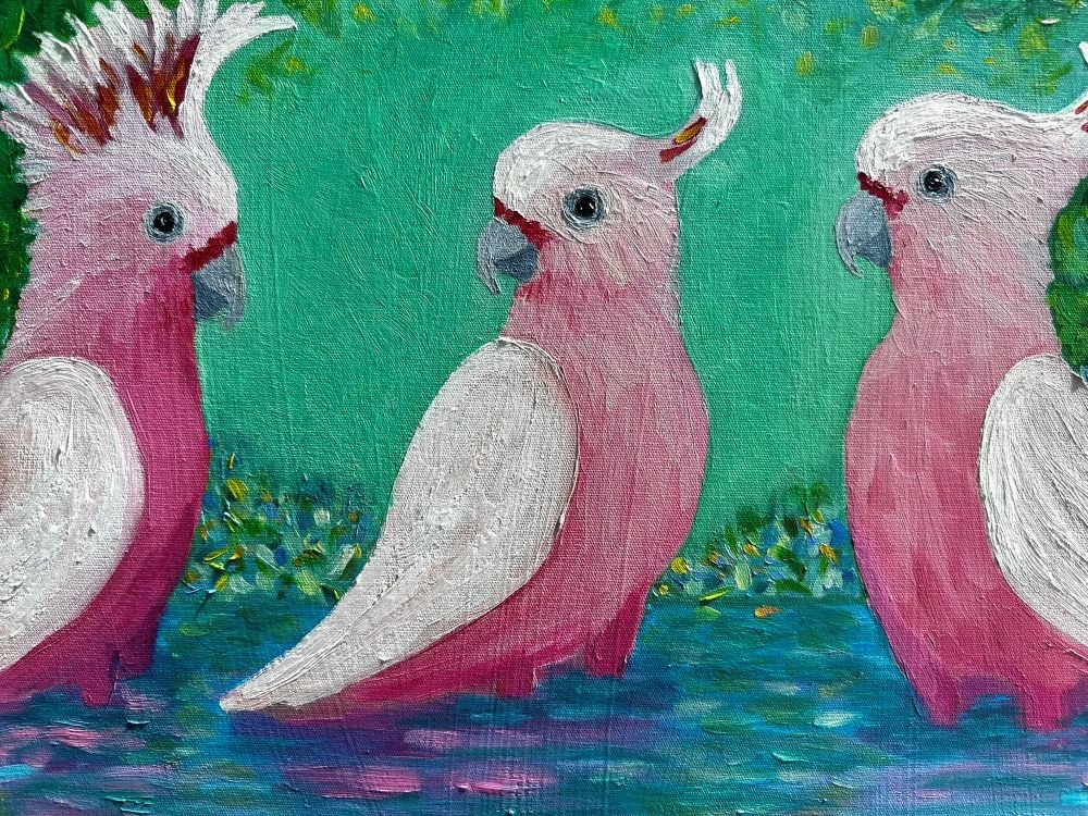Calm Pink Waters is an original oil painting by Australian artist Cassie Holmes, showing three Pink Cockatoos standing in water surrounded by yellow and blue flowers. Close up.