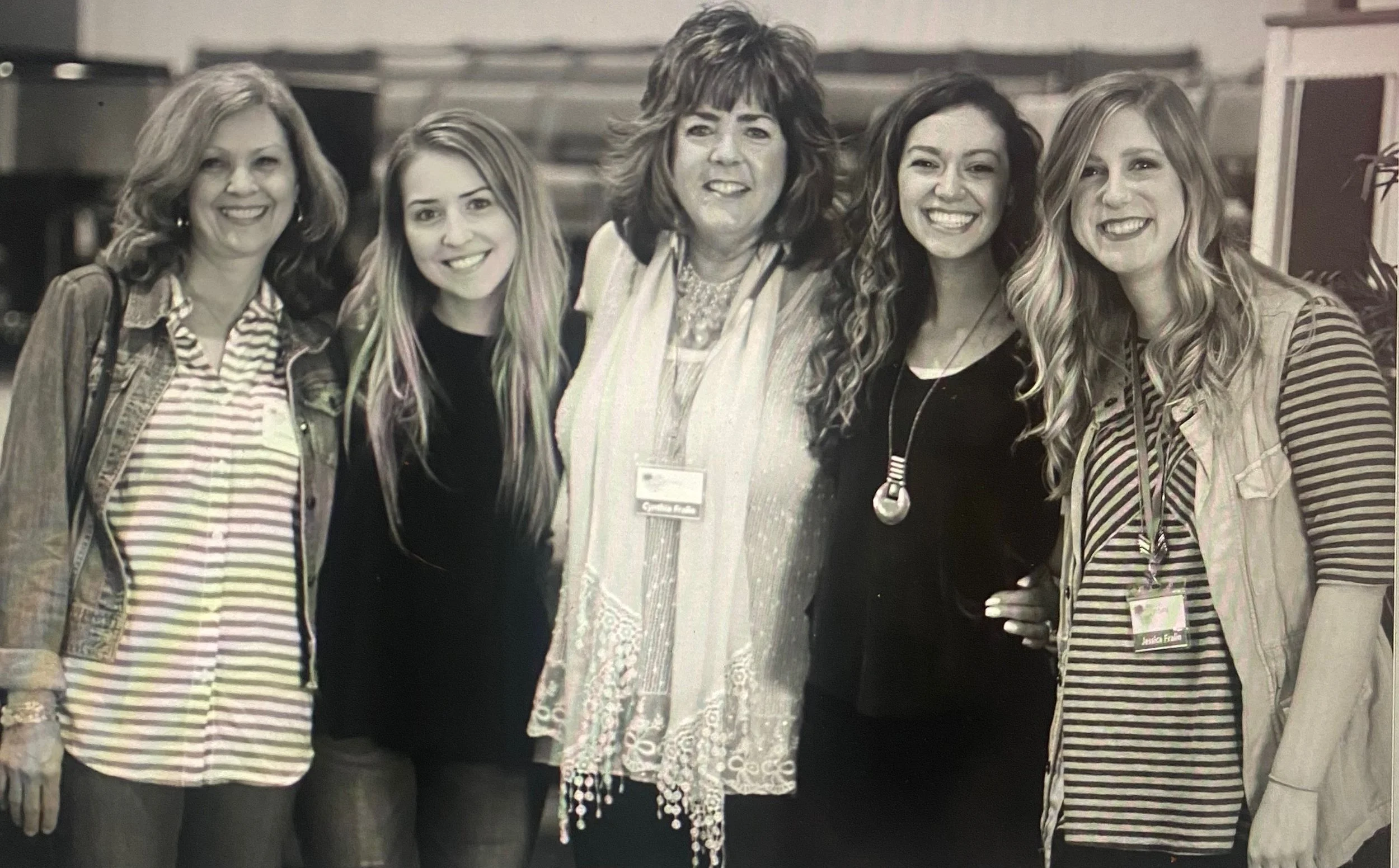 Group of five women posing and smiling for a photo indoors.