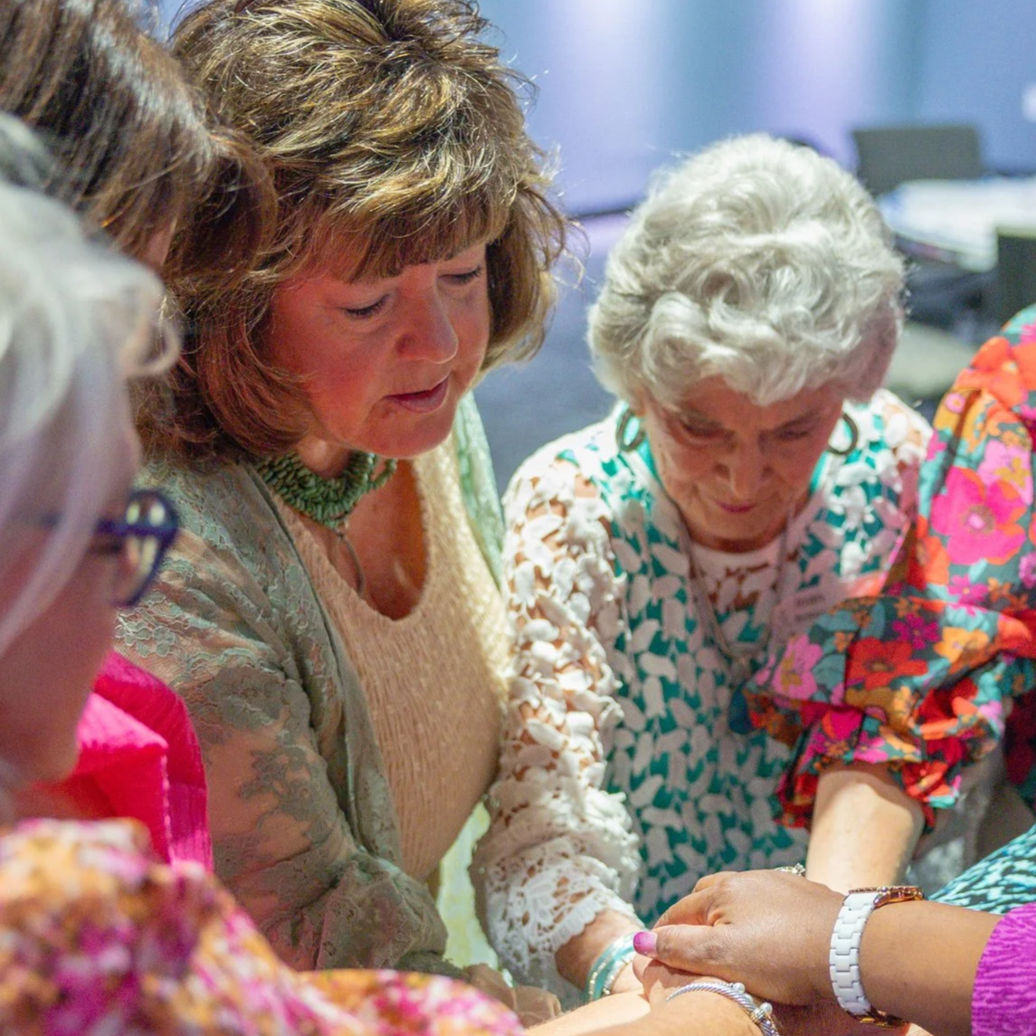 A group of women engaging in a close, intimate activity, possibly praying or participating in a ritual, with their hands joined or held together.