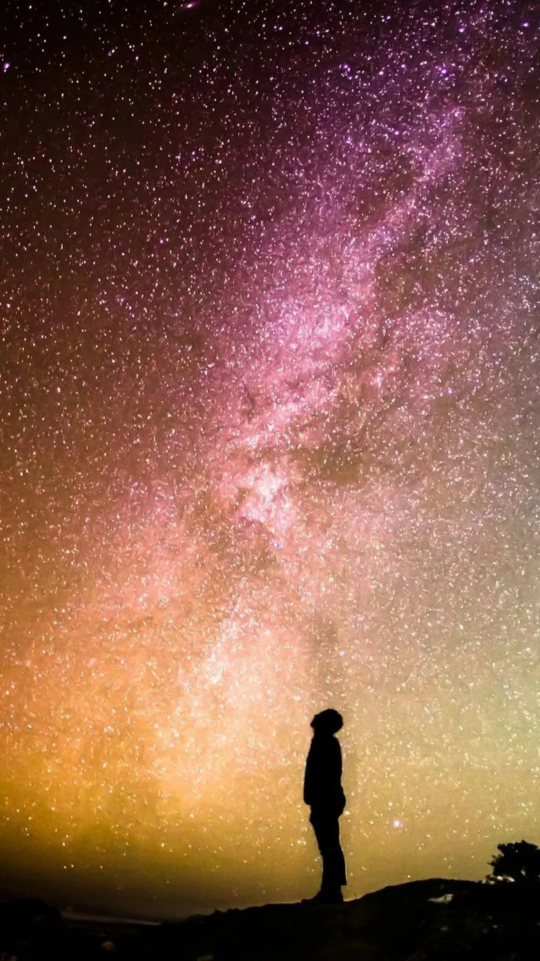 Silhouette of a person standing on ground at night with a clear view of the galaxy and stars in the sky.