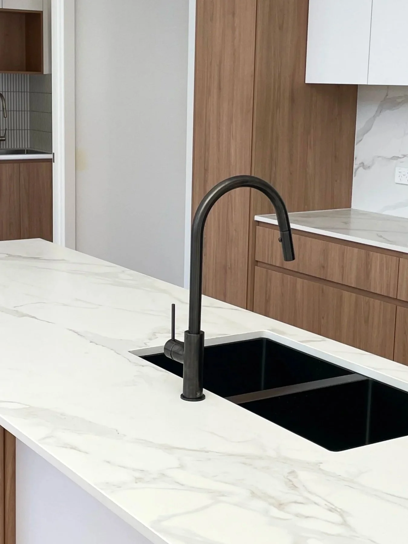 Modern kitchen with white marble countertop, black sink, black faucet, and wooden cabinets.