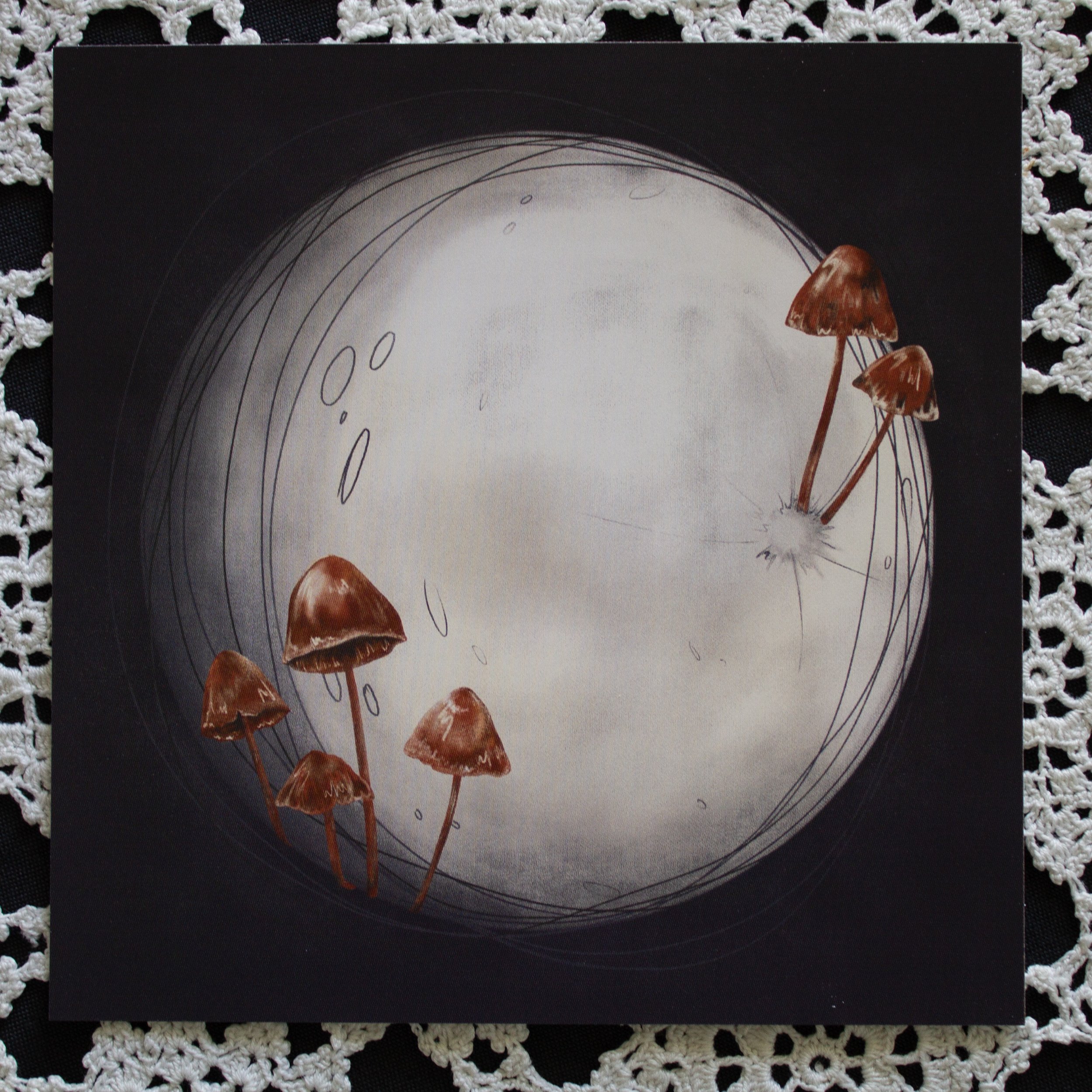 A postcard of mushrooms growing out of the moons surface placed on top of a lace cloth