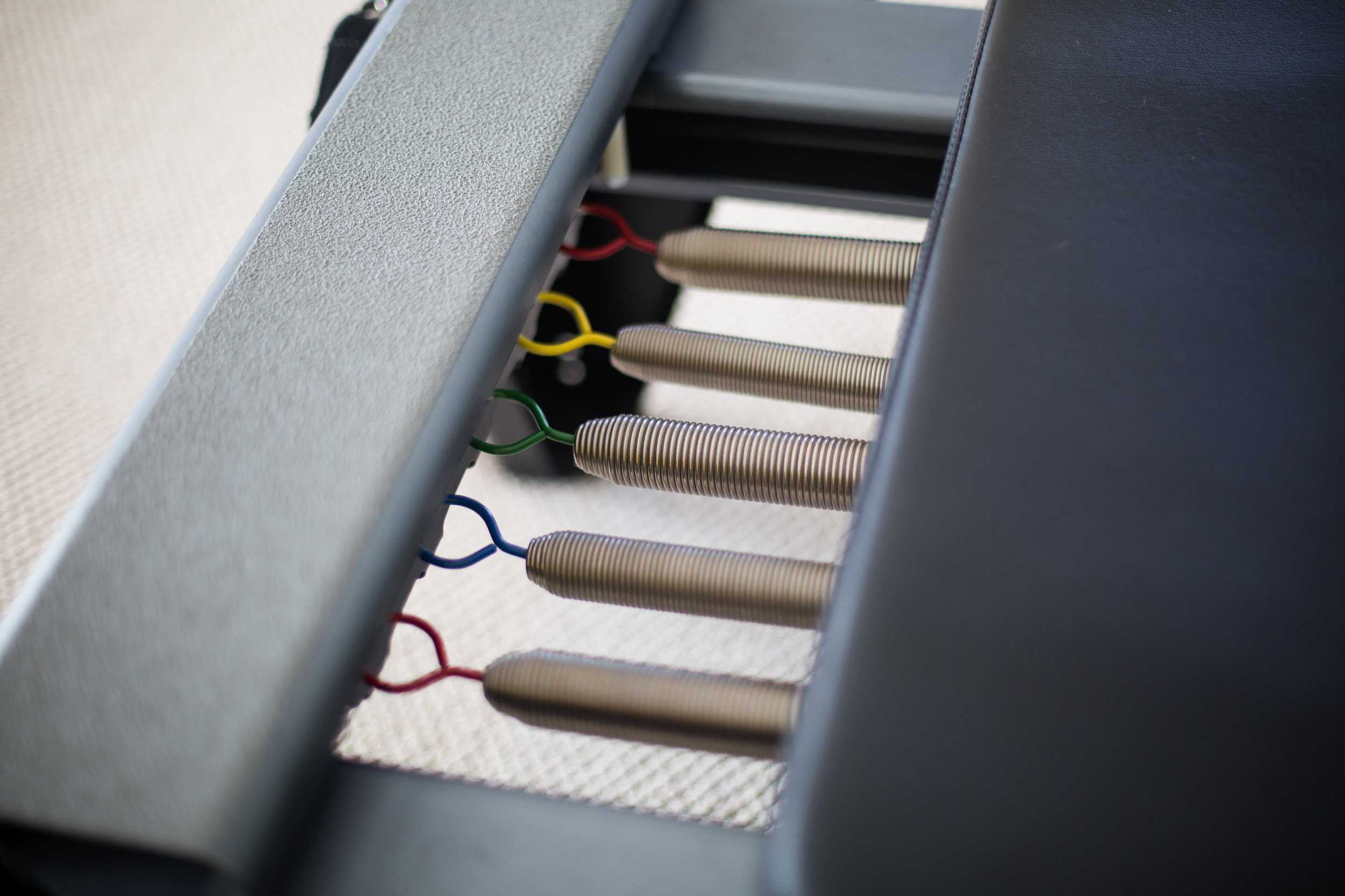 Close-up of a row of metal coil springs connected to colorful wires underneath a piece of furniture, possibly a bed or a sofa, showing the internal structure.