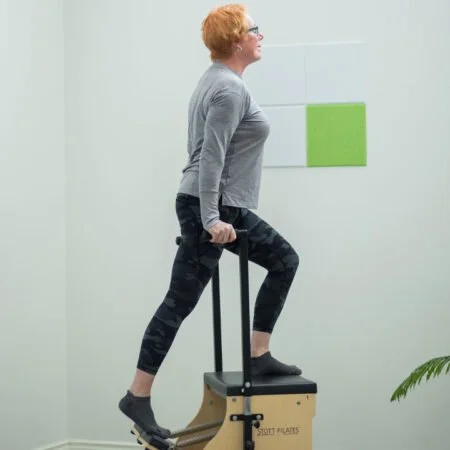 Woman performing a step-up exercise on a plyometric box in a fitness room.