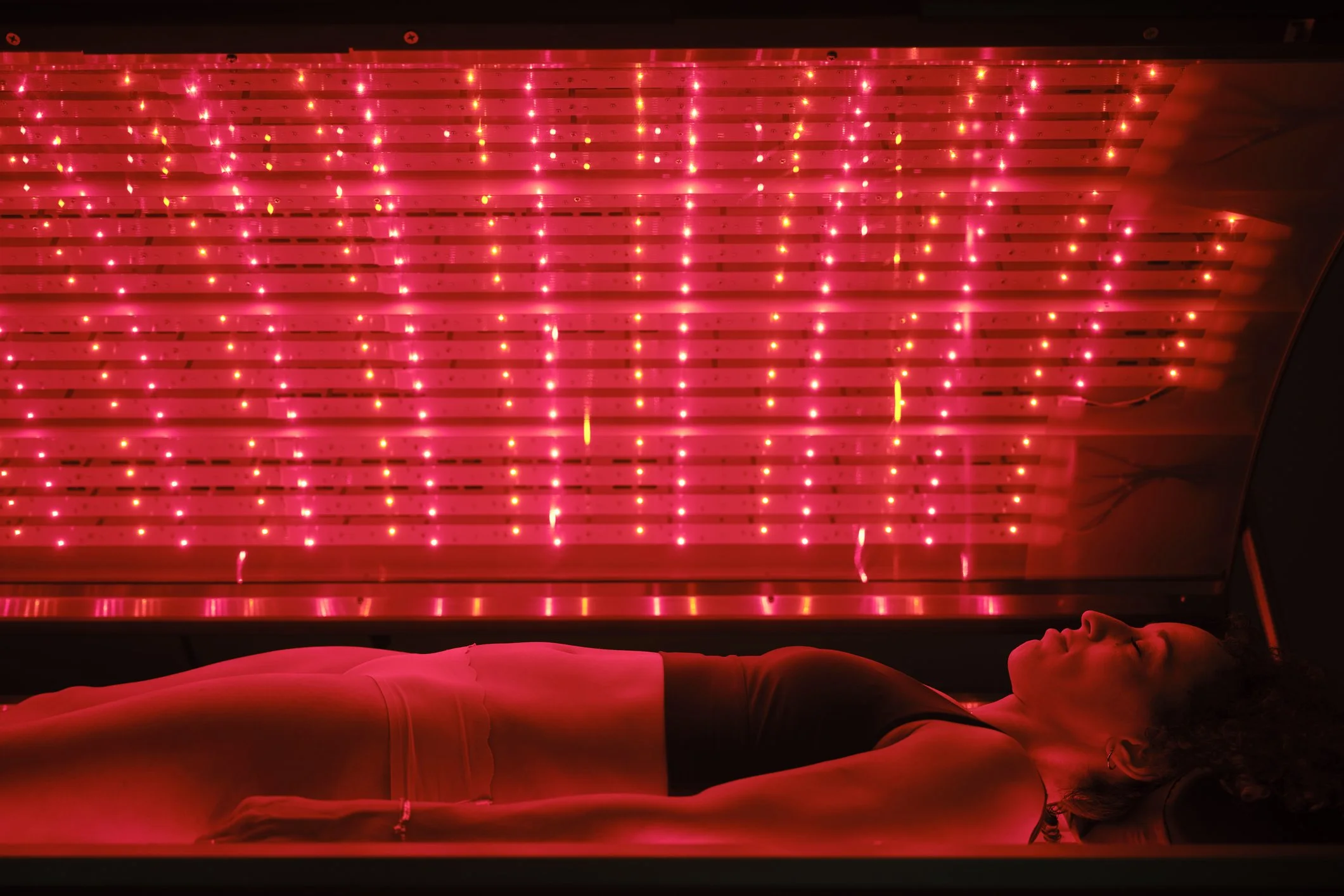 A person lying on a bed under red LED light panels with a futuristic design.