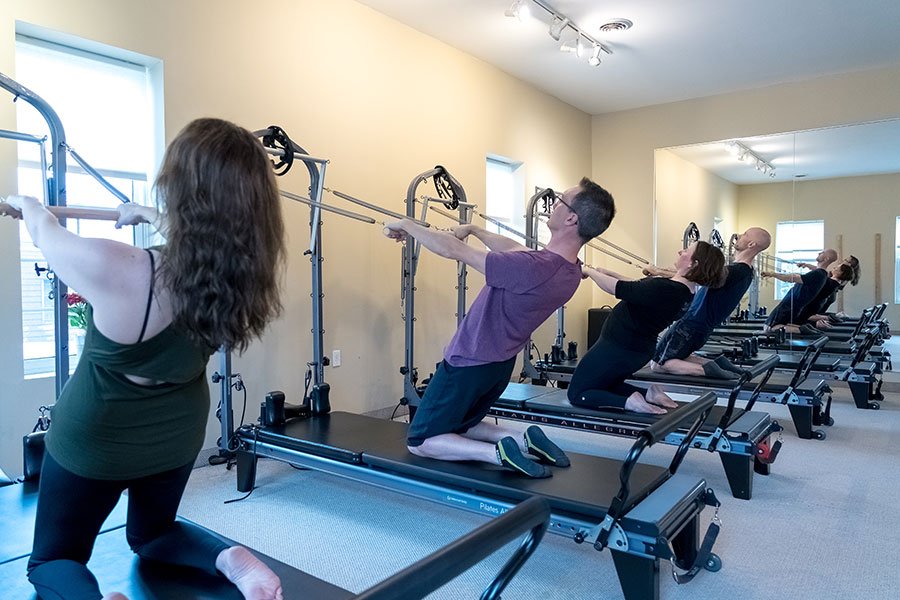 People participating in a Pilates class on reformer machines in a bright studio.