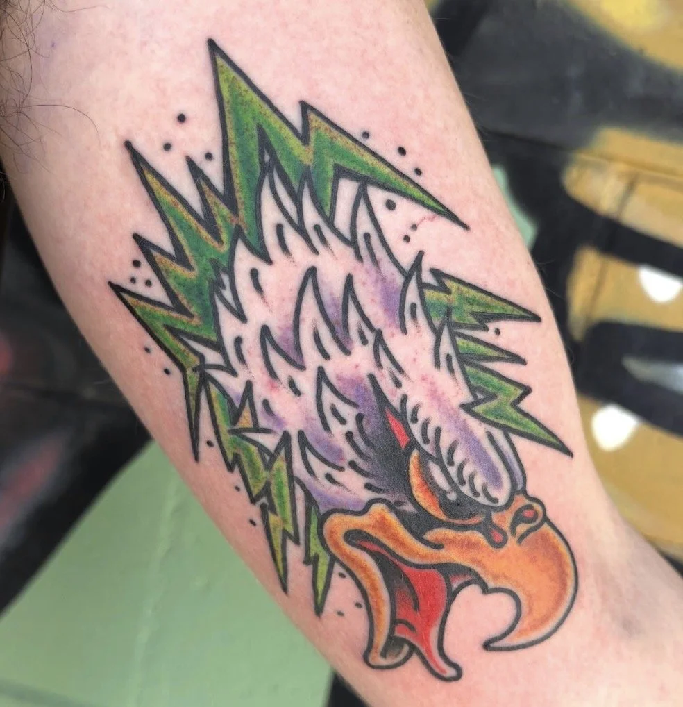 Colorful tattoo of a snarling dragon with green spikes, purple scales, orange features, and red flames on a person’s arm.
