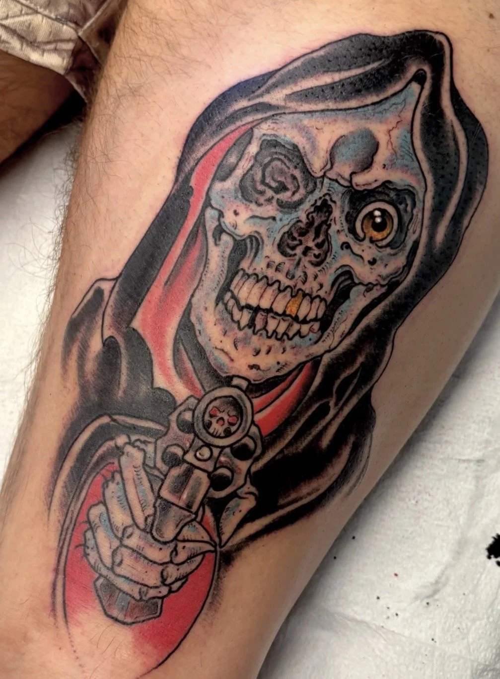 Detailed tattoo of a grinning skeletal figure in a hooded cloak holding a scythe, with red and black shading.