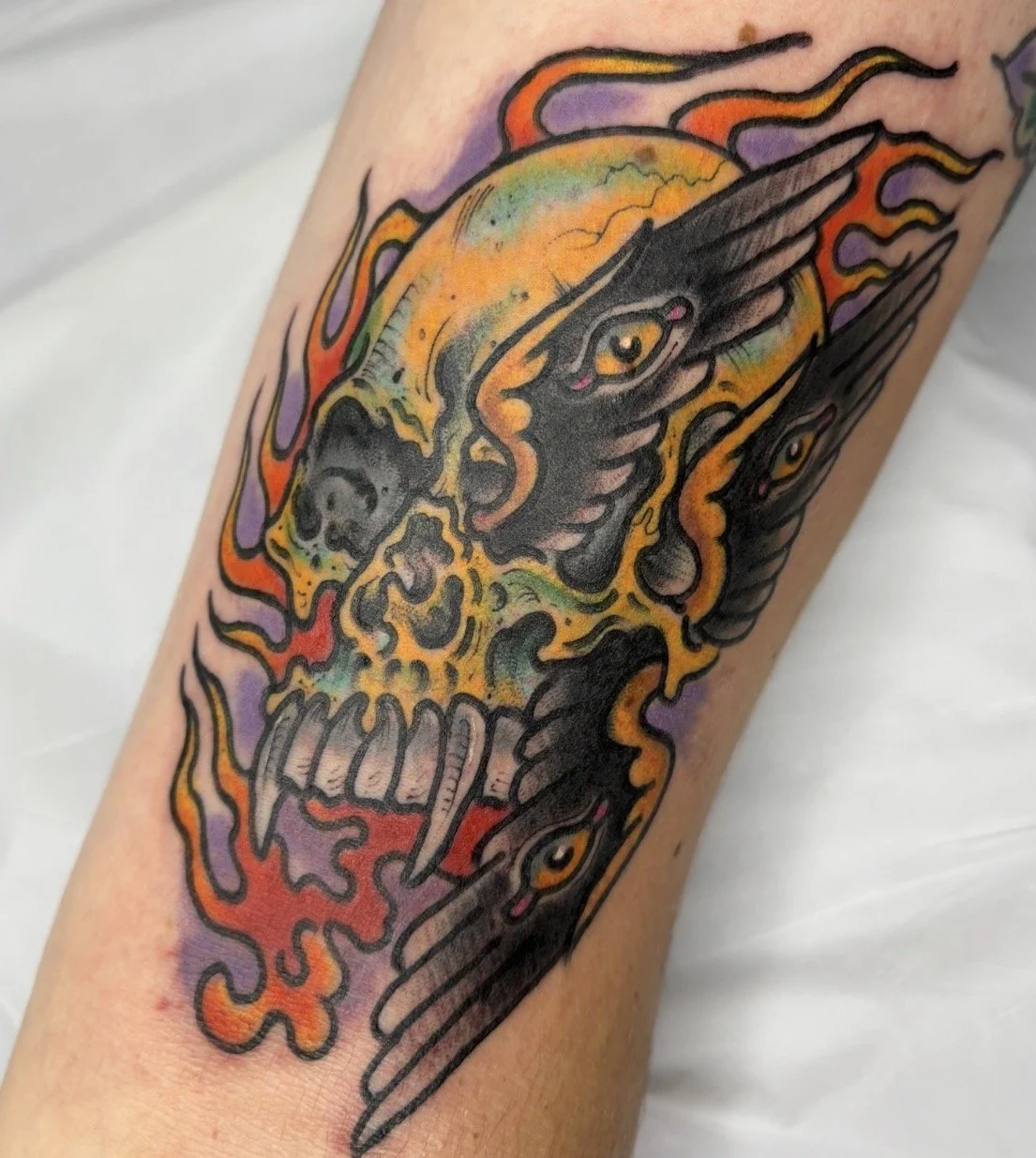 Colorful tattoo featuring a snarling skull surrounded by stylized black panthers, flames, and purple-orange accents.