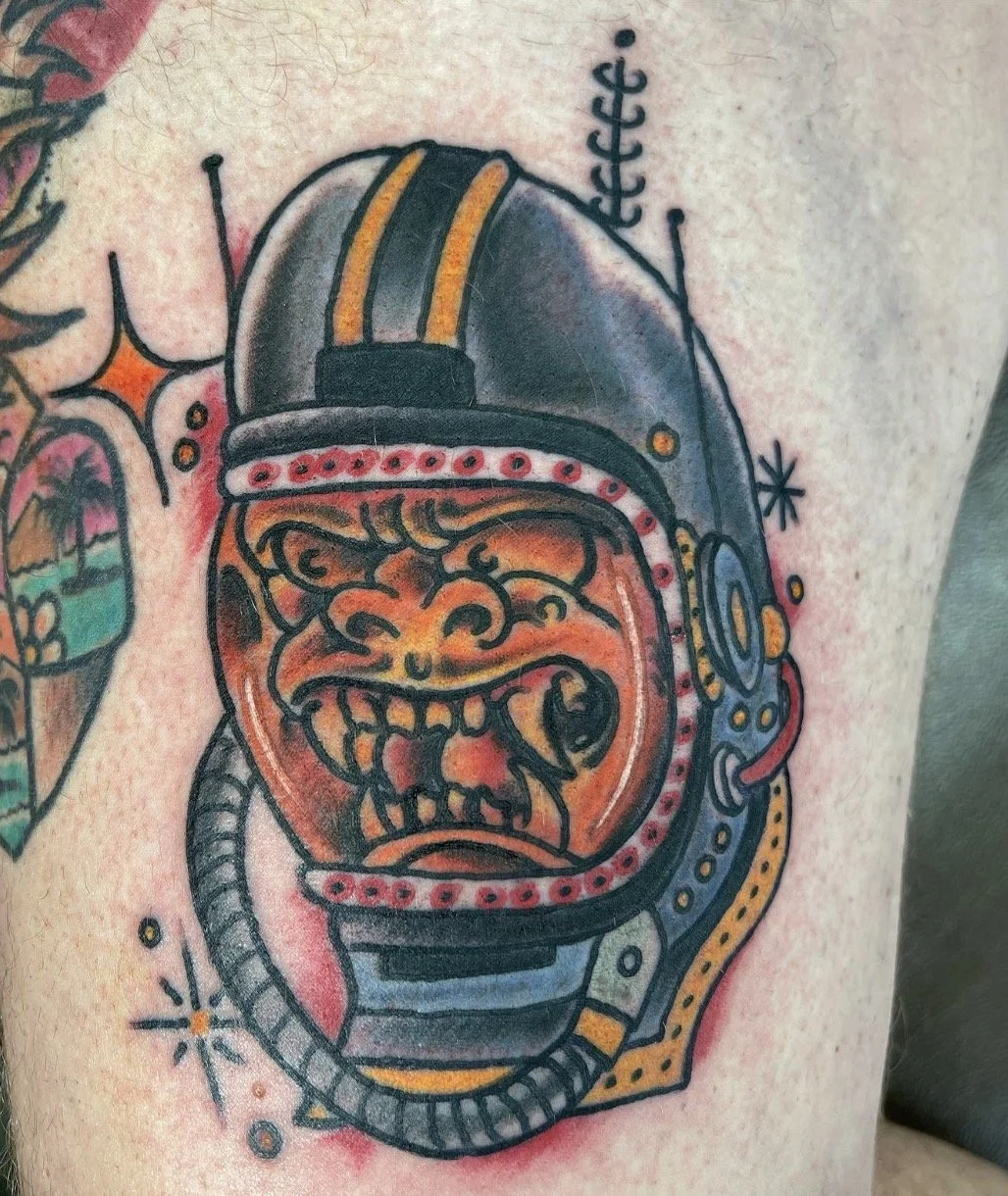 Colorful tattoo of a grinning, sharp-toothed monster wearing a domed helmet and armor