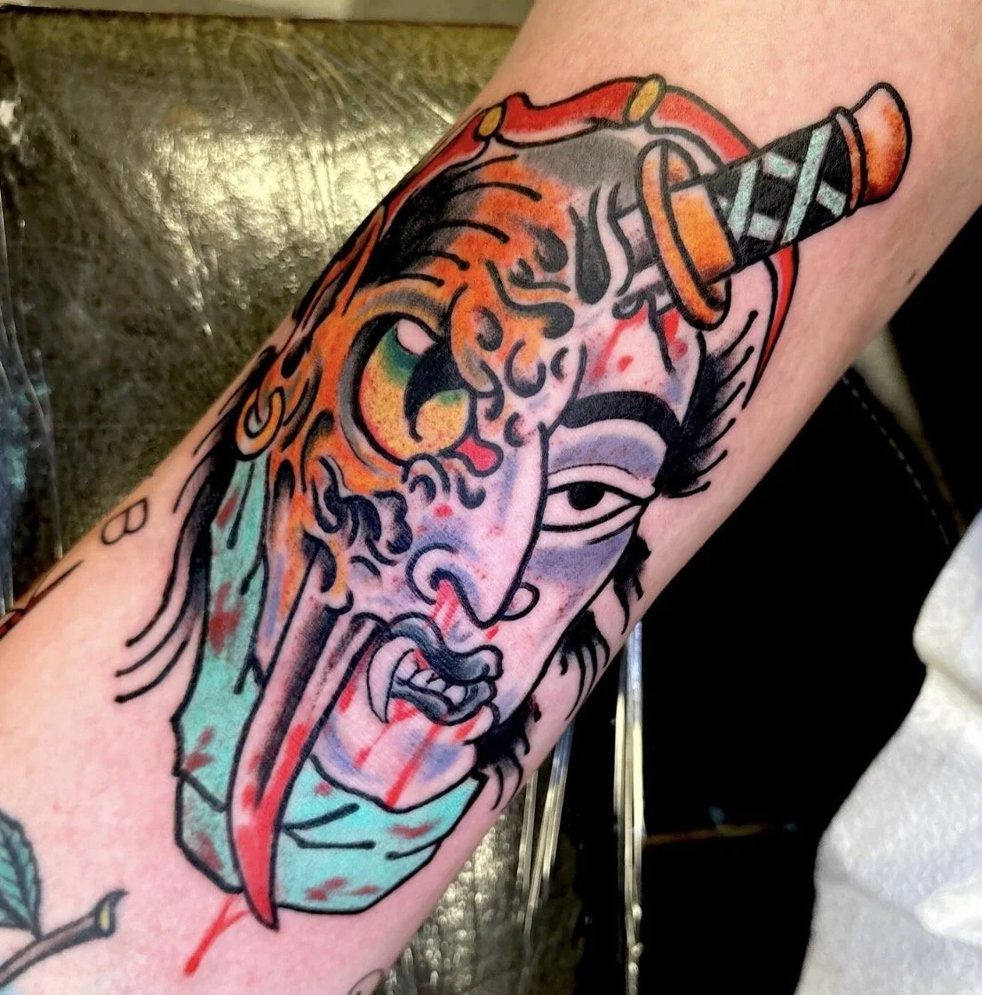 Colorful tattoo of a stylized bearded male face wearing a horned helmet on a forearm
