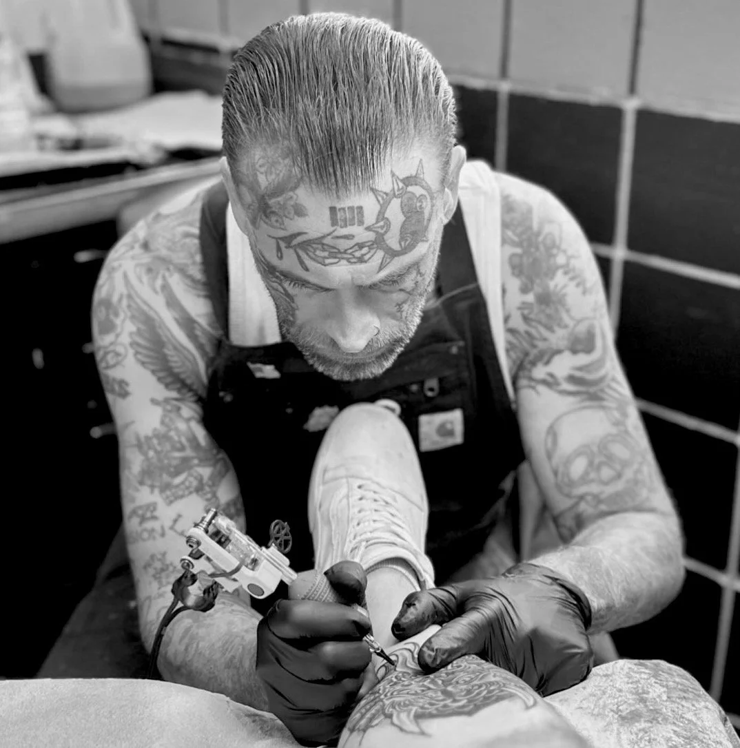 Tattoo artist wearing gloves tattoos a client’s leg in a studio.